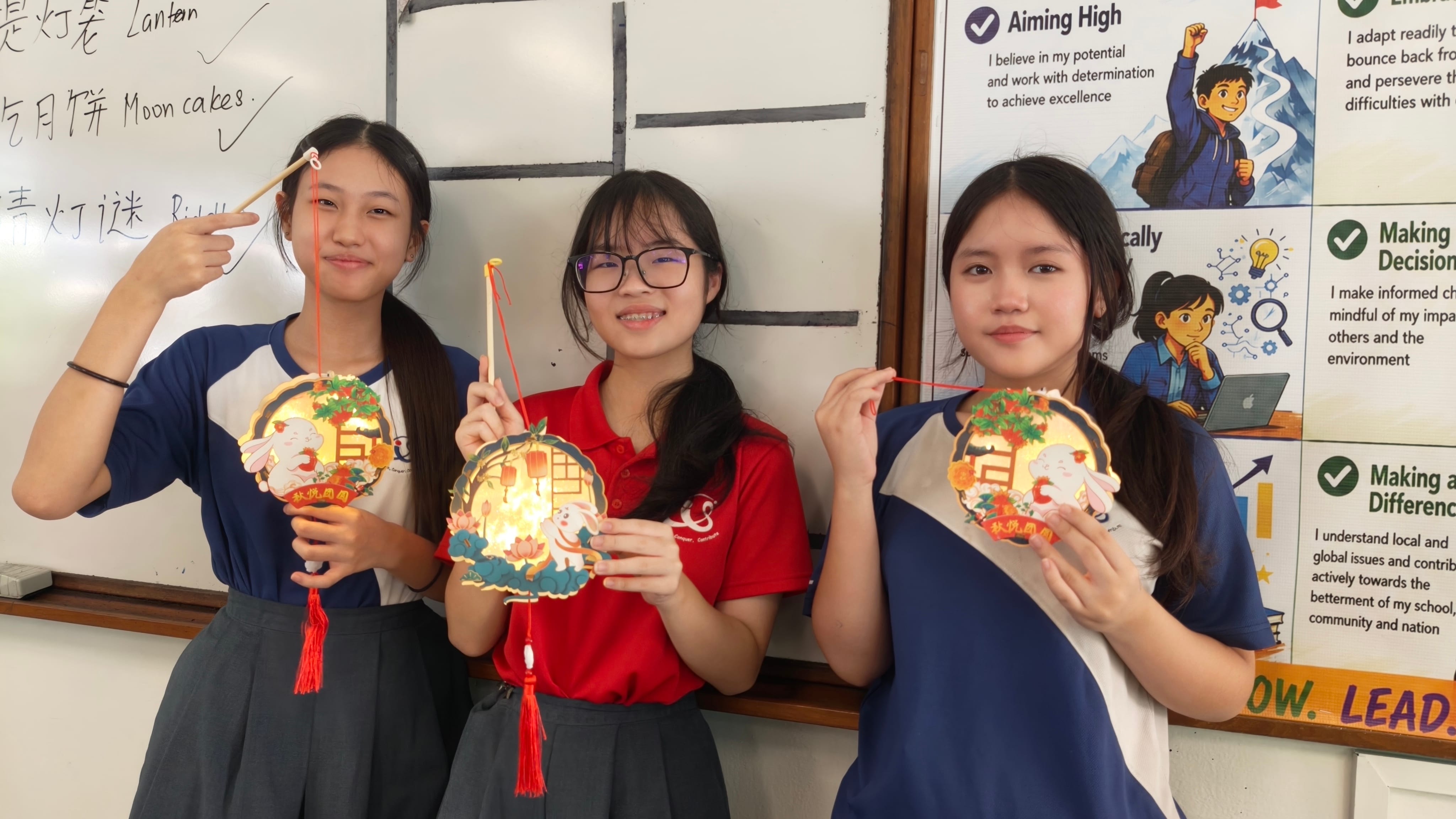 Three secondary school girls stand in front of a whiteboard with Chinese writing about Mid-Autumn Festival traditions. Each holds a glowing round lantern decorated with rabbit and lotus motifs, with Chinese text reading 秋情圆圆.